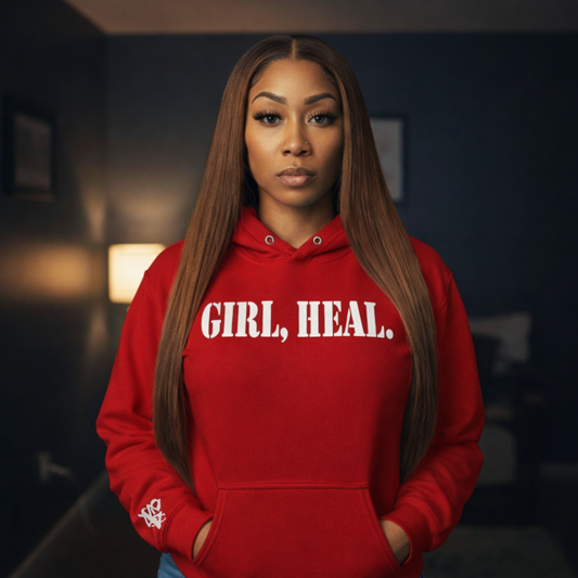 Person wearing a red hoodie with 'GIRL, HEAL.' text in a dimly lit room.